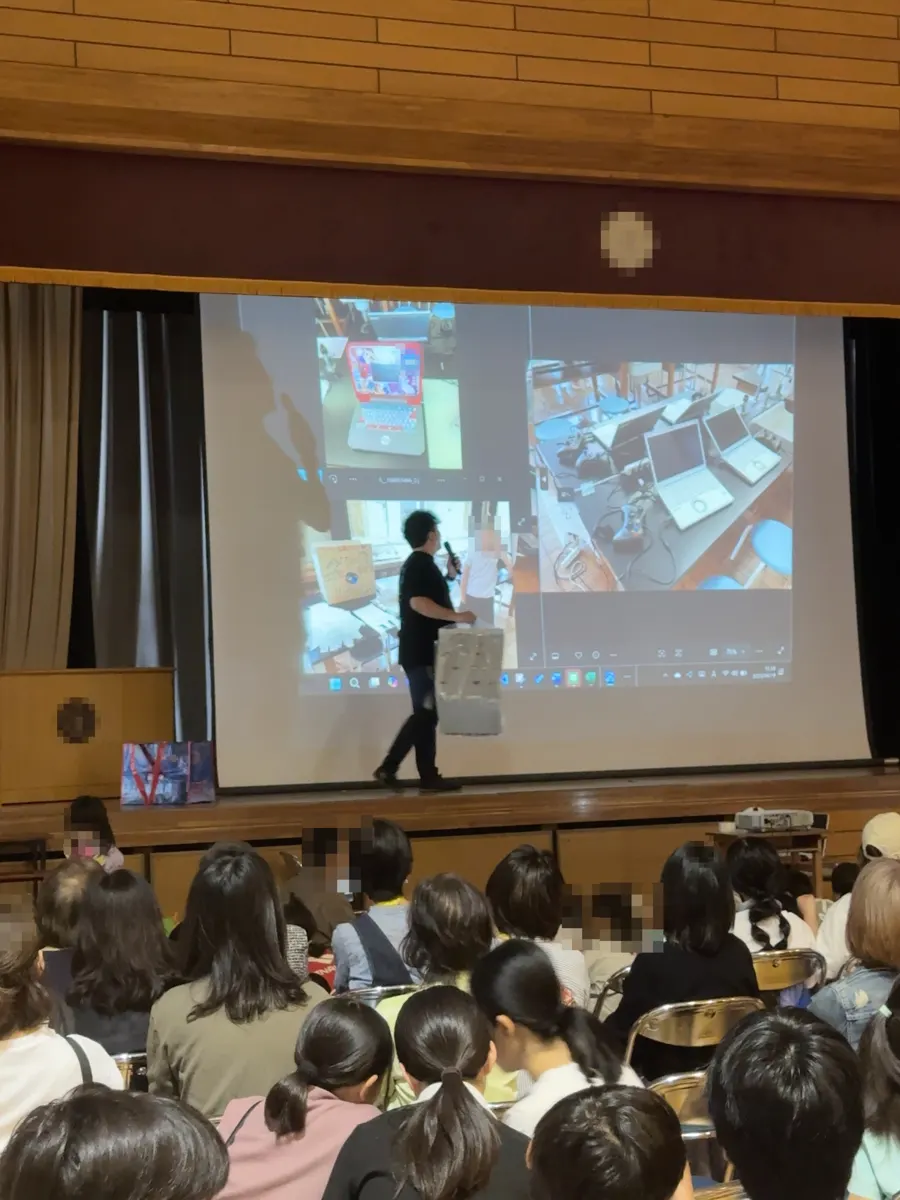 小学校の体育館で、子どもたちがスクリーンを見ながら話を聞いている様子