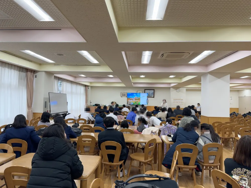 中学校のランチルームで、中学生や保護者がスクリーンを見ている様子